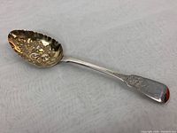 Side view of entire 9-inch sterling silver spoon showing floral design on handle and contours of repousse bowl with berry relief.