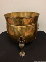 Front view showing oval shape, flared rim, claw feet, and one lion head handle with ring