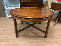 Round mid-century modern rosewood coffee table with cross stretcher base, showing natural wood grain and finish.