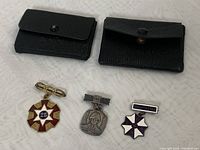 Overview of all three badges with two black pouches, showing size, color, and layout of items in the lot.