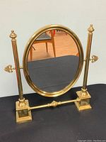 Front view of vintage brass vanity mirror showing oval shape, decorative finials, and polished brass frame.