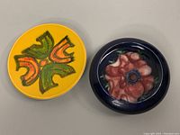 Two round pottery plates side by side, one yellow with abstract design and one navy with flower design