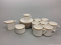 Full set arranged showing 8 mugs, 7 saucers, creamer, and sugar bowl with consistent gold rim.