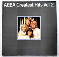 Front cover of Abba Greatest Hits Vol. 2 album. Black jacket with color photo of the band and white text title.