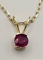 Close-up of the 14k gold chain with a small genuine ruby pendant showing the red faceted gemstone and gold prong setting.