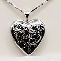 Heart-shaped sterling silver locket pendant on chain, showing engraved floral swirl pattern on front.
