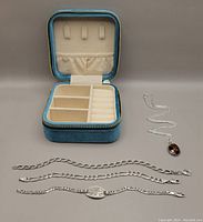Jewelry storage box with three silver bracelets laid out beside it, showing compartments and size.