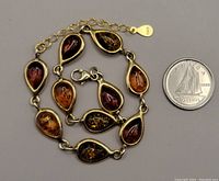 Close-up of the amber bracelet with its waterdrop-shaped amber stones in various colors and the 925 stamp visible on some stones and on the clasp. A Canadian dime is placed next to it for scale.