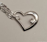 Open heart pendant and portion of chain on light grey background