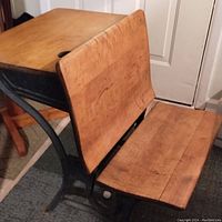 Side view of antique child's school desk showing solid wood seat, backrest, and desktop with wrought iron frame