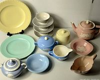 Wide shot of pastel ceramic serving pieces including plates, teapots, sugar bowls, creamers, cups and bowls arranged on a white surface