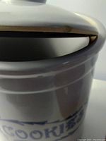 Close-up image showing chip and crack damage to the rim of the Marcrest cookie jar lid and body.