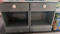 Front view showing two identical gray nightstands side by side with drawer and open shelf, surface scratches visible.
