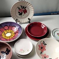 Overview of several pottery plates and bowls with pink floral design and colorful patterns on white table.