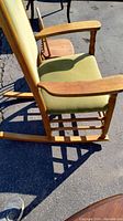 Side view of sage green upholstered rocking chair showing seat, armrest, wooden frame and partial child's chair behind
