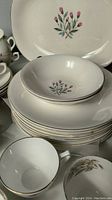 Stacked Wedgwood dinner plates and bowls with pink floral design and teacups visible