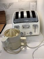 Avante four slice toaster with metal top and white plastic body, along with Braun juicer placed on a white countertop.