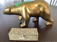 Side view of polished brass bear sculpture on flat surface with fabric-covered case positioned in front.