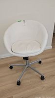 Front view of white faux leather Ikea swivel chair with caster wheels on a wood floor.