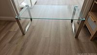 Clear view of the rectangular glass top coffee table showing the glass surface and polished metal legs from a top side angle.