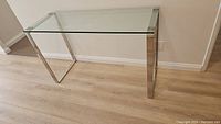 Full view angle of the glass top console table with metal legs on wooden floor.