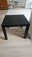 Front angle of black Ikea side table showing square top and four straight legs on light wood floor.