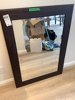 Full view of the rectangular mirror standing against a wall showing dark wood stained wide frame and bevelled glass edges.