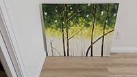 Image showing full canvas leaning against the wall with visible green, yellow, and white painted tree scene.