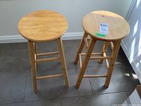 Two pine wood stools shown side by side on a tiled floor with natural light from a window.