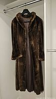 Full view of dark brown sheared beaver fur coat, hanging on a hanger showing the front and side with collar and long sleeves.