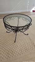 Front angled view of vintage side table showing metal ornate base with scrollwork and round glass top.