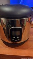 Front view of rice cooker showing stainless steel body and digital control panel with buttons.