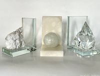 Set of three bookends showing white crystal geode, white alabaster block with alabaster sphere, and large clear crystal diamond-shaped prism on glass bases.