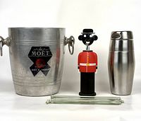 Wide frontal image showing the Moet & Chandon ice bucket, Queens Guard corkscrew, stainless steel cocktail shaker, and glass cocktail stir sticks laid horizontally in front.
