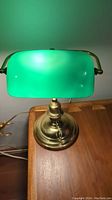 Front angle of the banker’s lamp highlighting the green glass shade and brass base with visible wear.