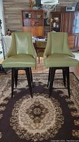 Pair of green vinyl upholstered bar stools positioned on a decorative rug inside a room with wooden furniture and decor.