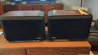 Pair of Bose Series IV speakers side by side showing wood laminate tops with some peeling and black corner protectors