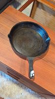 Top-down angled view showing the entire cast iron skillet on a wooden surface, highlighting the cooking surface and handle.