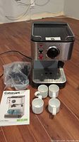 Full set including Cuisinart espresso maker, four white ceramic cups, milk frother attachment parts in plastic bag, and instruction manual.