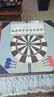 Front view of the new classic dartboard in box including darts with blue and red flights shown on the box art.