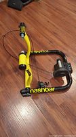 Side view of Nashbar fluid resistance direct drive indoor bike trainer on wooden floor, showing the black and yellow frame with resistance unit and adjustment knobs.