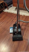 Full view of Miele canister vacuum with power beater brush head on hardwood floor, showing body and attached hose.