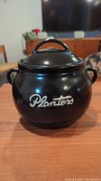 Front view of the black ceramic Planters peanut jar with the Planters logo visible.