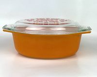 Side view of vintage orange Pyrex oval casserole dish with clear glass lid on top showing the shape and color of the dish.