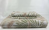 Folded queen size quilt with tropical leaf pattern showing cream background and muted green, brown leaves arrangement.