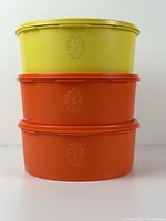 Stacked view of three oval containers, two orange and one yellow, each with a floral emblem on the side, to show condition and design.