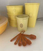 Front view of stacked yellow Tupperware containers with floral design and orange measuring spoons arranged in front.