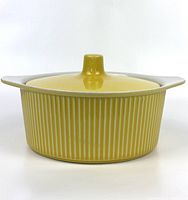 Front-side view of vintage canary yellow ribbed baking casserole with lid, showing glossy finish and cream-colored handles.