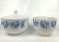 Front view of both milk glass bowls showing blue floral pattern. Larger bowl has lid with knob.