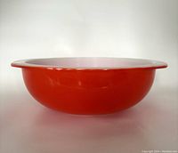 Side view of the bright red orange Pyrex bowl showing smooth rounded shape and wide flared rim
